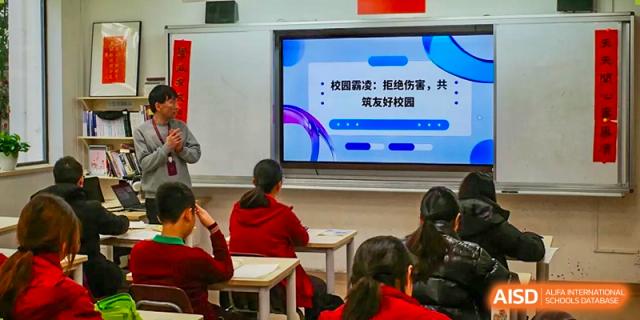 Students from Shanghai Concord Bilingual School sit at their desks, looking at a presentation on a screen at the front of the classroom.