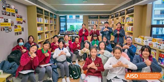 Students from Shanghai Concord Bilingual School sit on the floor and pose for a group photo in a library.