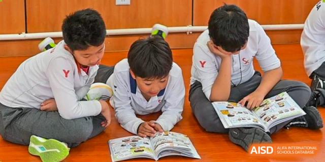 A young male student from Shanghai Concord Bilingual School reads a book, with other students sitting around him.