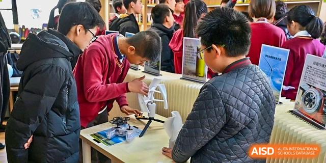 A group of male students from Shanghai Concord Bilingual School gather around a table, looking at a small robot.
