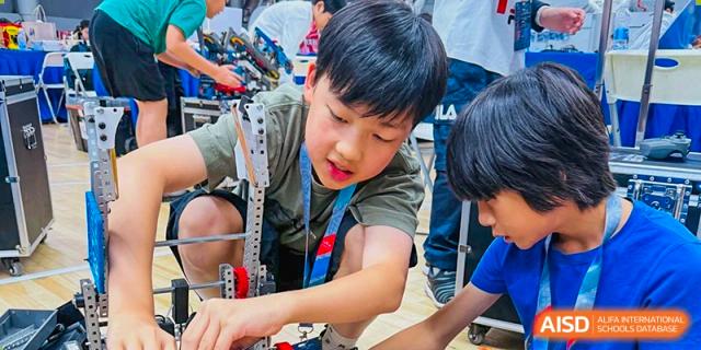 A male student from Shanghai Concord Bilingual School works on a robotics project with various parts and tools.