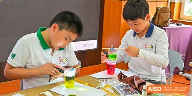 Two students from Shanghai Concord Bilingual School are conducting a colorful science experiment with liquids in a cup.