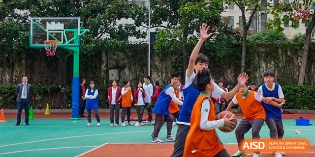 A group of students from Shanghai Concord Bilingual School are playing basketball, with one student reaching to block a shot.