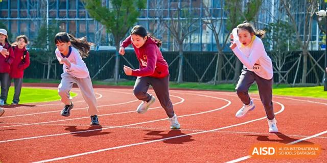 A female student from Shanghai Concord Bilingual School runs on a red track during a sports event.