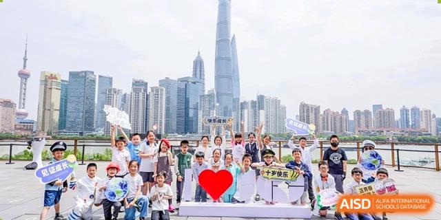 A large group of students and adults from Shanghai Concord Bilingual School pose for a photo with a city skyline in the background.