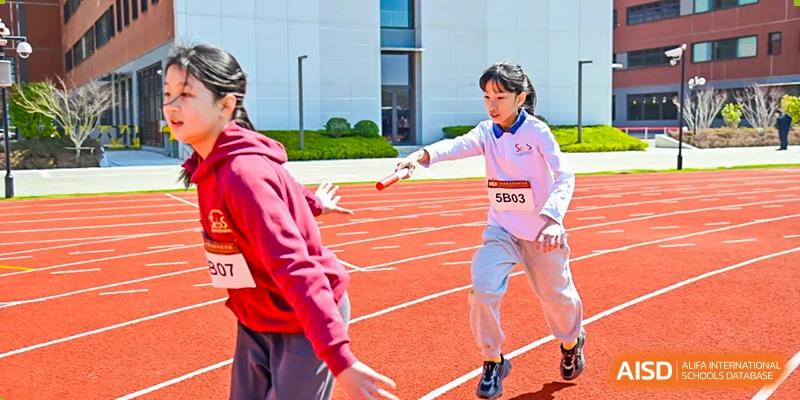 A female student from Shanghai Concord Bilingual School runs on a track and holds a baton during a relay race.