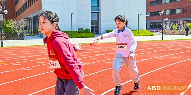 A female student from Shanghai Concord Bilingual School runs on a track and holds a baton during a relay race.