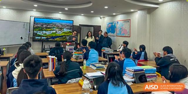 Students and a teacher gathered around a central table for a group discussion in a modern classroom at Wuxi Guanghua School.