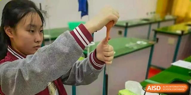 A student's hand holding a piece of lab equipment or a chemical reagent during a science experiment at Wuxi Guanghua School.