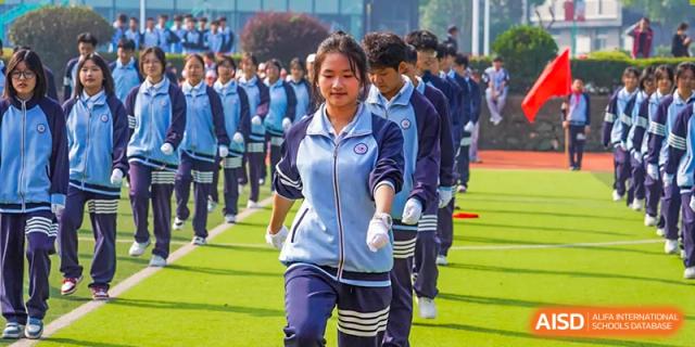 A female student leading a line of students in blue and white uniforms outdoors at Wuxi Guanghua School.