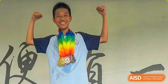 A smiling student holding up a fist and wearing rainbow-colored medals, celebrating success at Wuxi Guanghua School.