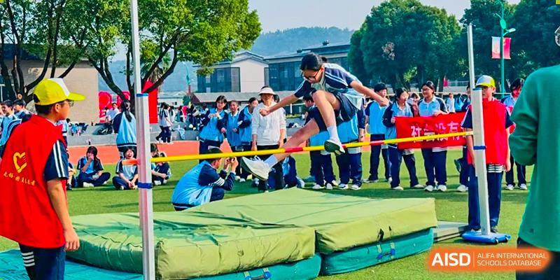 A student performing a high jump over a bar onto a cushioned landing mat during a sports day at Wuxi Guanghua School.