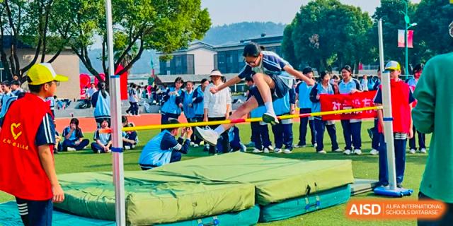 A student performing a high jump over a bar onto a cushioned landing mat during a sports day at Wuxi Guanghua School.