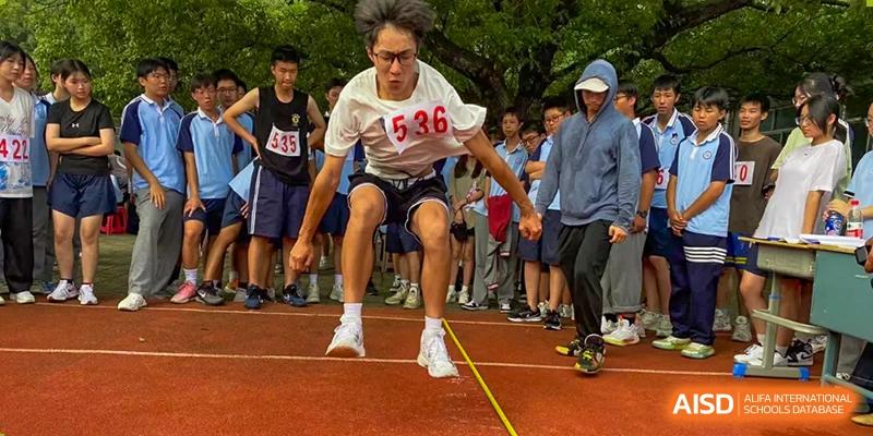 A male student performing a long jump or triple jump during an athletics competition at Wuxi Guanghua School.