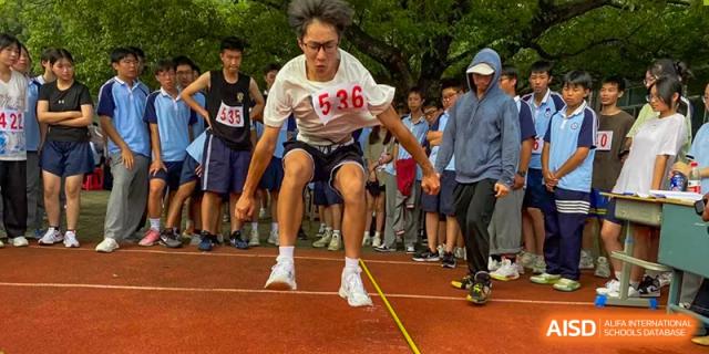 A male student performing a long jump or triple jump during an athletics competition at Wuxi Guanghua School.