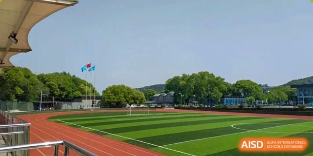 A sunny view of the outdoor sports field with a green turf area and running track at Wuxi Guanghua School.