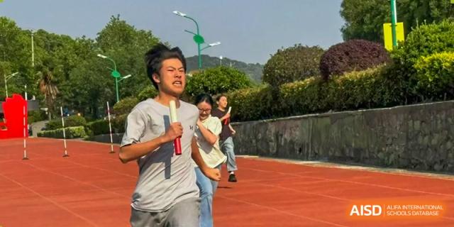A male student running on the track with a microphone during a sports day event or race at Wuxi Guanghua School.