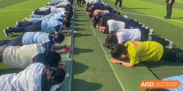 Students performing push-ups or an exercise outdoors on a green turf field during physical training at Wuxi Guanghua School.