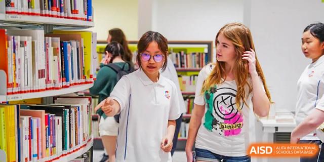 Students from Beijing Lize International Academy stand and look at books in a library or media center.