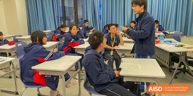 Students from Beijing Lize International Academy sit at a desk and look at a mobile device.