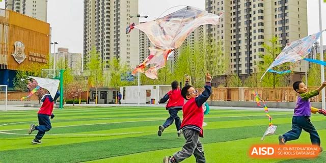 Students from Beijing Lize International Academy play and cheer on a green field with a building in the background.
