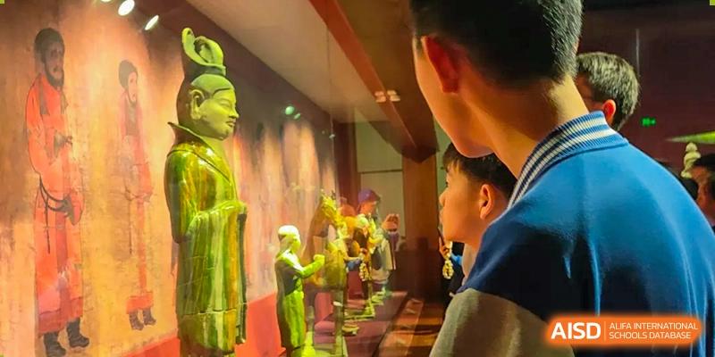 A group of students from Beijing Lize International Academy watches a golden statue in a museum with bright lights.