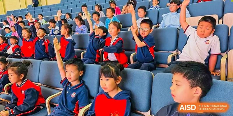 A group of students from Beijing Lize International Academy raises their hands in a classroom or auditorium setting.