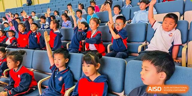A group of students from Beijing Lize International Academy raises their hands in a classroom or auditorium setting.