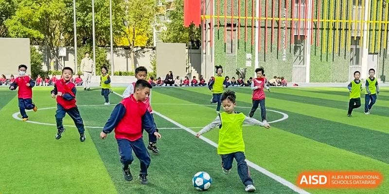 Students from Beijing Lize International Academy play soccer on a green field with a fence in the background.