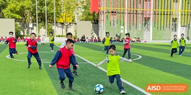 Students from Beijing Lize International Academy play soccer on a green field with a fence in the background.