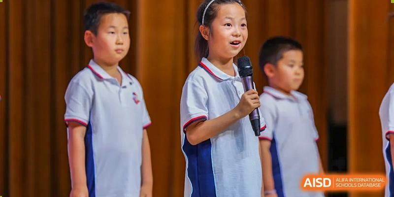 Two students from Beijing Lize International Academy, one with a microphone, sing or speak on a stage.