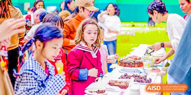 A Canadian International School of Beijing female student in a red uniform looks at a table full of desserts.