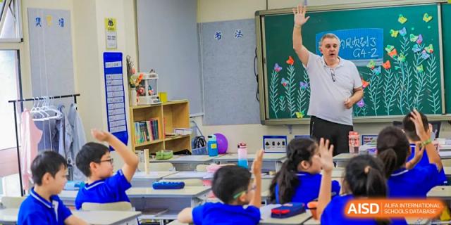 A teacher in a classroom with a student whose hand is raised at Beijing Mingcheng Academy.