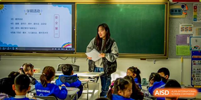 A teacher standing in front of a large whiteboard, giving a lesson to students at Beijing Mingcheng Academy.