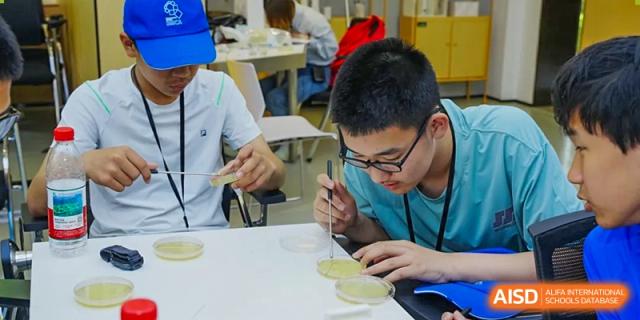 Students in a lab with microscopes or other science equipment at Beijing Mingcheng Academy.