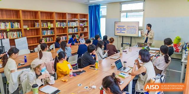 A group of students working together on a project at tables in a library at Beijing Mingcheng Academy.