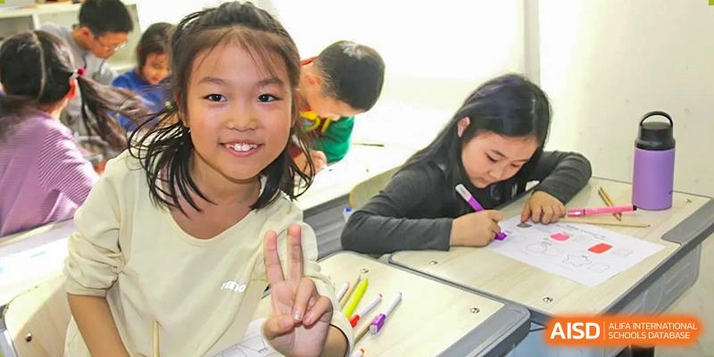 A young student smiling and doing schoolwork at a desk at Beijing Mingcheng Academy.