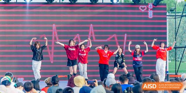 A group of students performing a dance on a stage for an audience at Beijing Mingcheng Academy.