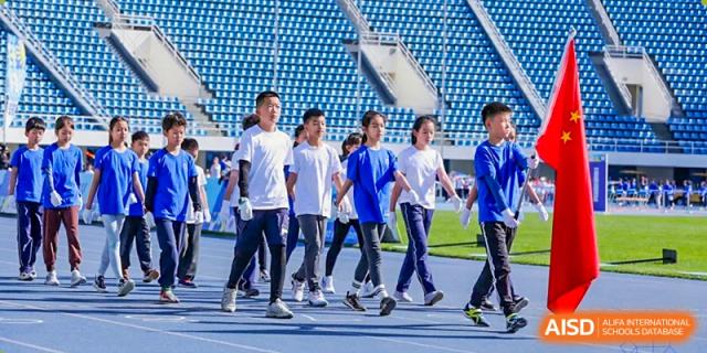 A group of students in blue and white tracksuits marching together on a running track at Beijing Mingcheng Academy.