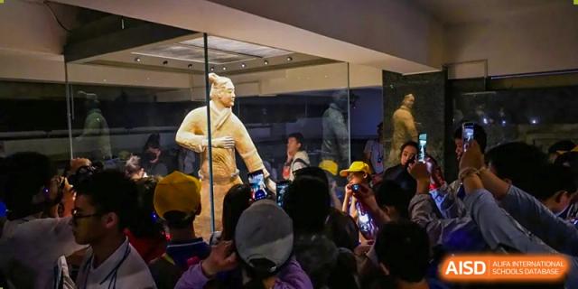 A crowd of people gathered around a statue or exhibit at Beijing Mingcheng Academy.