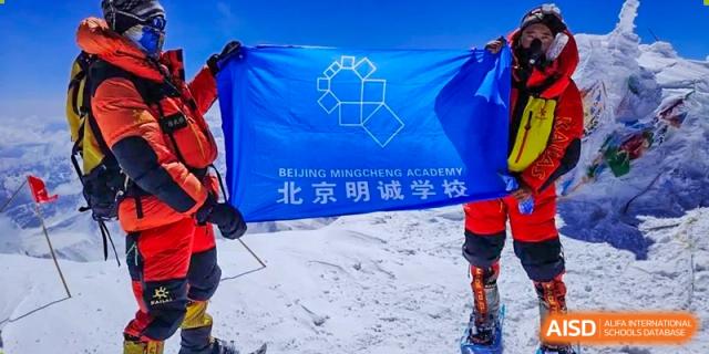 Two students in winter clothing holding a banner that says "Beijing Mingcheng Academy".