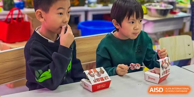 Two young students eating food from takeout boxes at Beijing Mingcheng Academy.