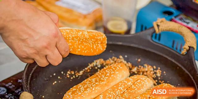 A close-up of a hand holding a piece of baked bread or pastry with sesame seeds at Beijing Mingcheng Academy.