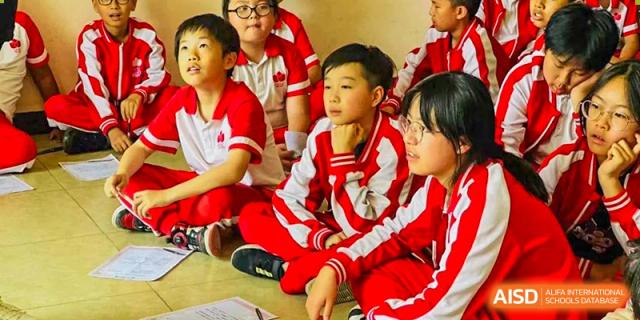 Students from Kunming Concord College of Sino-Canada (CCSC) in red uniforms sit together on the floor during class.