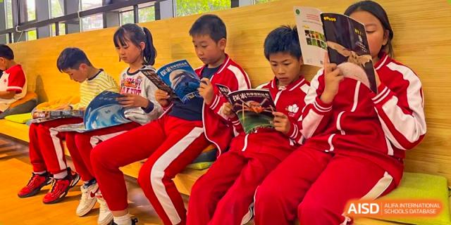 Two students from Kunming Concord College of Sino-Canada (CCSC) in red uniforms sit at a desk and work on a project together.