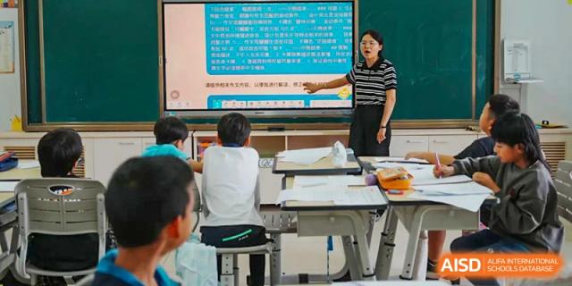 A student from Kunming Concord College of Sino-Canada (CCSC) is seated in a classroom while a teacher points to a diagram on a screen.