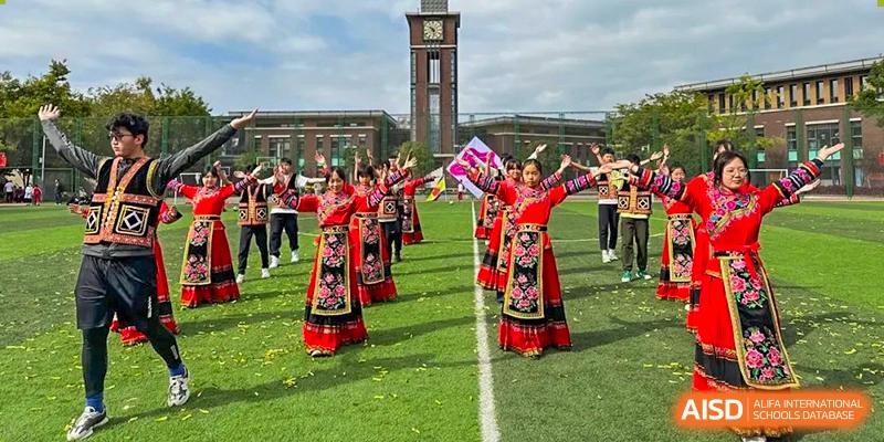 Kunming Concord College of Sino-Canada (CCSC) students in traditional red outfits pose for a photo on a sports field with a clock tower in the background.