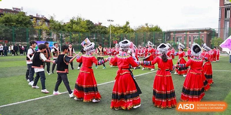 Students from Kunming Concord College of Sino-Canada (CCSC) perform a traditional dance in red costumes on a sports field.