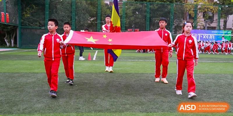 A student from Kunming Concord College of Sino-Canada (CCSC) holds a large Chinese flag during an event on the field.