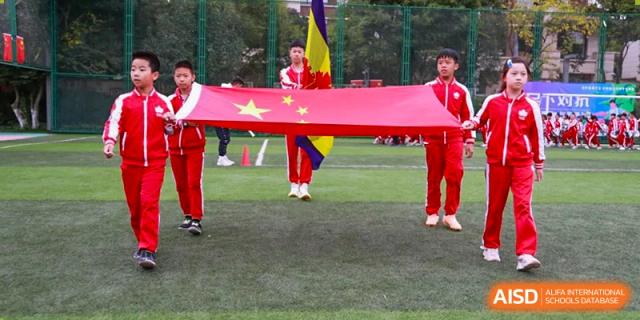 A student from Kunming Concord College of Sino-Canada (CCSC) holds a large Chinese flag during an event on the field.